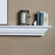 a white mantle with books and a candle on it next to a framed photograph in a brown room