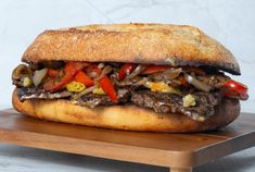 a sandwich with meat, peppers and onions on a cutting board