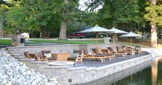 lounge chairs and umbrellas are set up on the edge of a lake in front of a stone wall