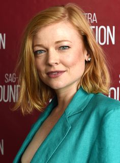 a woman with blonde hair wearing a blue suit and smiling at the camera while standing in front of a red backdrop