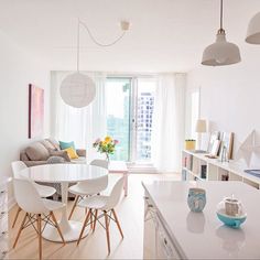 a white kitchen and living room with an open floor plan, dining table, chairs, bookshelves, windows, and artwork on the wall