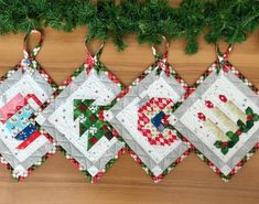 three quilted christmas ornaments hanging from a tree branch on a wooden surface with pine needles