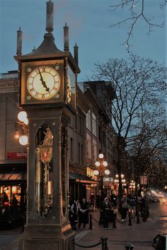 a clock tower in the middle of a city street at night with people walking around