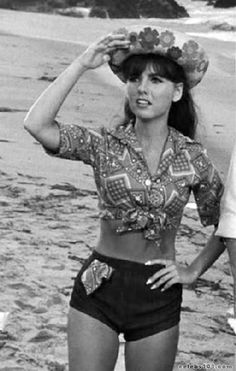 a woman standing on top of a sandy beach next to the ocean wearing a hat