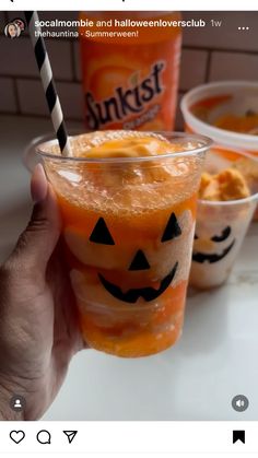 someone is holding up a halloween drink in front of two cups filled with orange juice