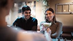 a man and woman sitting at a table with drinks in front of them, smiling