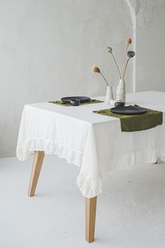 a white table with two plates on it and flowers in vases at the top