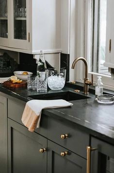 a kitchen with white cabinets, black counter tops and gold pulls on the faucet