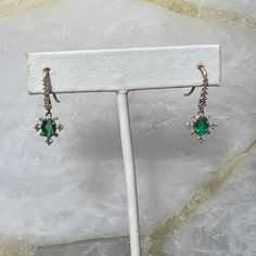 Unique epic hook earrings that add the perfect amount of elegance and sparkle to any look. Featuring stunning oval cut green Emeralds with a radiant diamond halo and diamond studded hooks above the emerald charm for perfect movement. The Vita earrings are sure to be a conversation starter and a treasured heirloom. Emeralds measure 5.8mm x 4mm and total diamond weight is 0.594 carats. Elegant Green Jewelry With Halo Design, Elegant Green Jewelry With Halo, Elegant Green Halo Jewelry, Elegant Earrings With Diamond Accents For May Birthstone, Elegant May Birthstone Earrings With Diamond Accents, Elegant Green Diamond Earrings, Elegant Diamond Earrings For May Birthstone, Elegant Emerald Diamond Earrings, Elegant Earrings With Halo Setting For May Birthstone