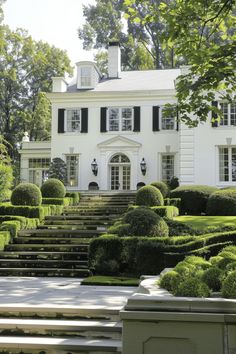 a large white house surrounded by trees and bushes with steps leading up to the front door