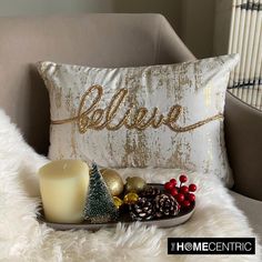 a candle and some christmas decorations on a chair next to a pillow that says believe