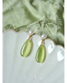 a pair of green and white earrings sitting on top of a shell next to a piece of cloth