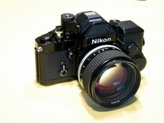 a nikon camera sitting on top of a white table next to a black lens