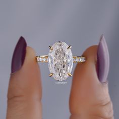 a woman's hand holding an oval diamond ring