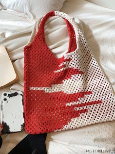 a red and white bag sitting on top of a bed next to a cell phone