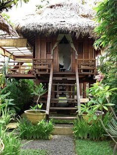 a wooden house with a thatched roof surrounded by greenery