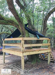 a wooden bench under a tree with a tarp on it's back end