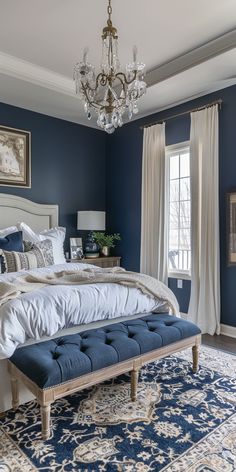 a bedroom with blue walls, white bedding and a chandelier hanging from the ceiling