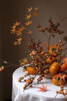 a table topped with lots of oranges and other autumn decorating items on top of a white cloth covered table