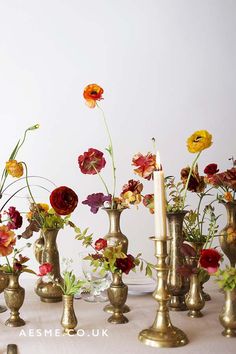 a table topped with lots of vases filled with flowers next to a lit candle