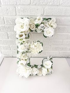 the letter e is made up of white flowers and greenery in front of a brick wall