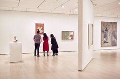 three people looking at art on display in an art gallery with white walls and wooden floors