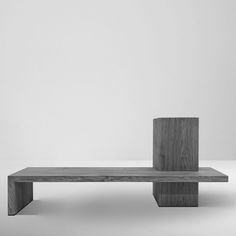 a wooden bench sitting on top of a white floor in front of a gray wall