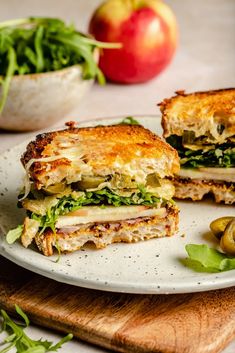 a sandwich cut in half sitting on top of a white plate next to an apple