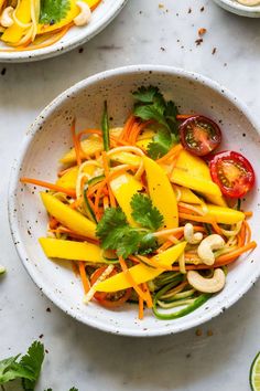 two white bowls filled with vegetables on top of a marble counter next to limes