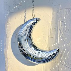 a mosaic moon hanging from a chain on a wall with white paint and light reflecting off it's surface