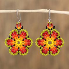 a pair of beaded earrings hanging from a wooden hook on a clothes line with a brown background