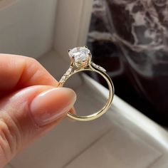 a hand holding a diamond ring in front of a window