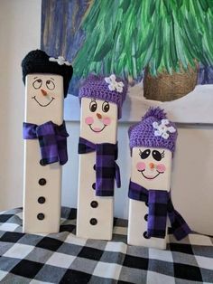 three wooden snowmen with hats and scarves are sitting on a checkered tablecloth