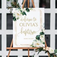 a welcome sign with white flowers and greenery on an easel in front of a black and white tiled wall