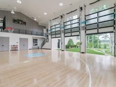 an indoor basketball court with hard wood flooring and glass doors leading to the upper level