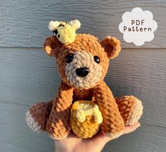 a small crocheted teddy bear is held up in front of a wooden wall