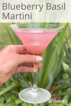 a hand holding a pink drink in a glass with the words blueberry basil martini