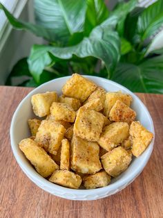 a white bowl filled with tofu sitting on top of a wooden table next to a potted plant