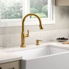 a kitchen sink with a gold faucet and white counter top next to a window