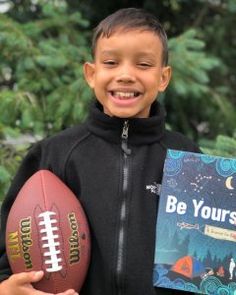 a young boy holding a football in his hand and a book about be yourself written on it