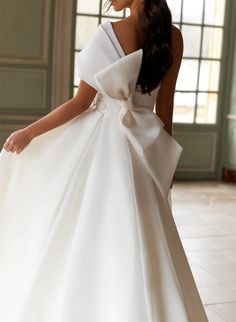 a woman in a white dress with a big bow on her shoulder