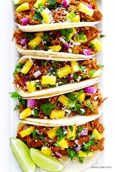 three tacos with pineapples, onions and cilantro on a white plate