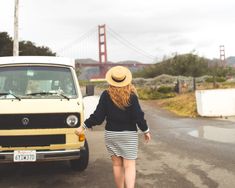 a woman walking down the road with her hat over her head and a yellow van in the background