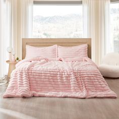 a bed with pink comforter and pillows in front of a window