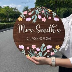 a woman holding up a wooden sign that says mrs smith's classroom