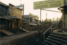 an old town with lots of wooden buildings and signs on the side of it,