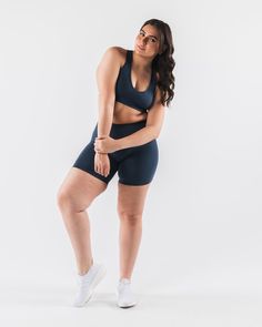 a woman in a black sports bra top and shorts poses for the camera with her hands on her hips