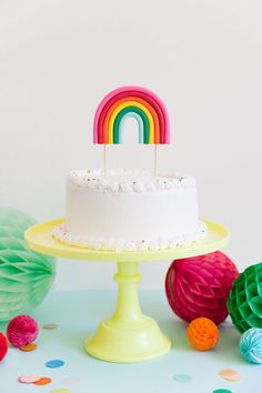 a white cake sitting on top of a table next to paper balls and rainbow decorations