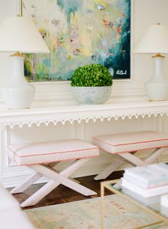 a white table with two benches and a painting on the wall behind it in a living room