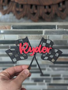 a hand holding up a red and black flag shaped cake topper that says ryder